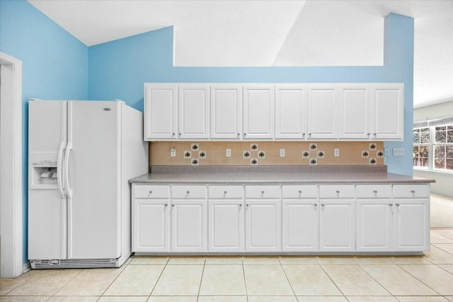 kitchen with white fridge with ice dispenser, light tile patterned flooring, and white cabinets