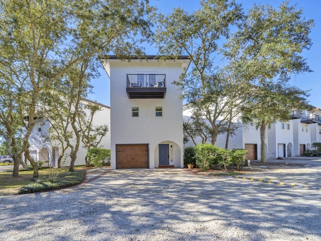 view of front of home featuring gravel driveway, a balcony, an attached garage, and stucco siding