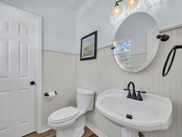 bathroom featuring toilet, a wainscoted wall, a sink, and wood finished floors