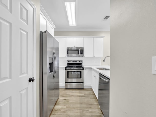 kitchen with stainless steel appliances, ornamental molding, a sink, and white cabinets