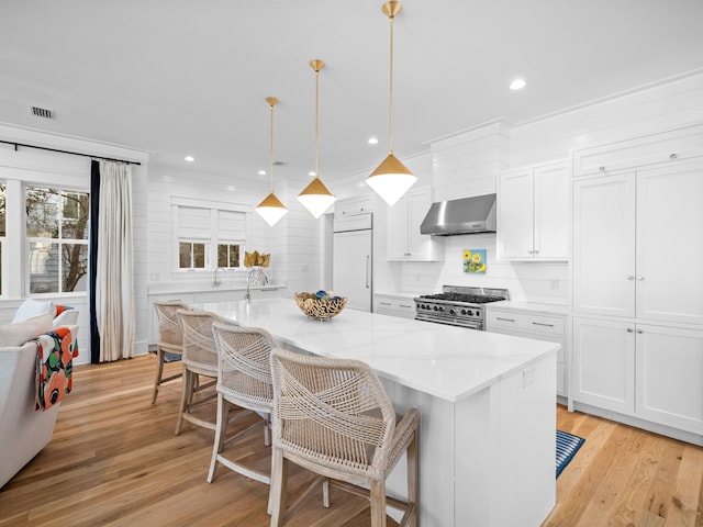 kitchen featuring light wood-style flooring, high end appliances, white cabinets, and wall chimney range hood