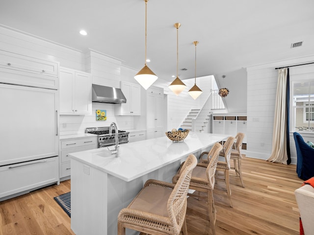 kitchen featuring a kitchen bar, light wood-style flooring, wall chimney exhaust hood, white cabinetry, and high end appliances