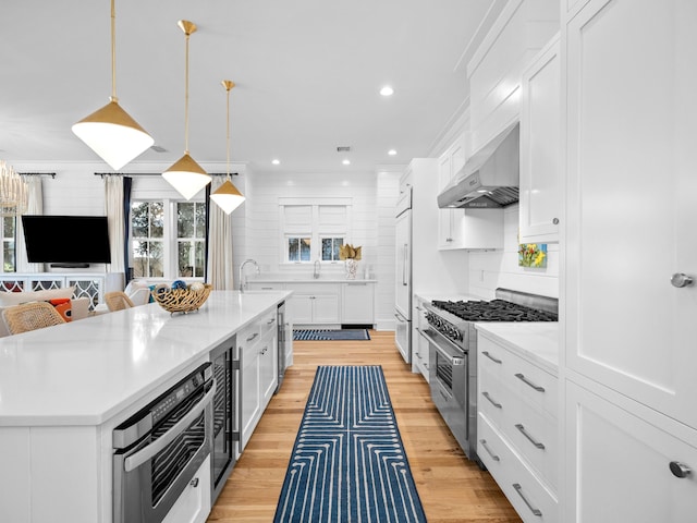 kitchen featuring white cabinetry, high quality appliances, wall chimney exhaust hood, and light countertops