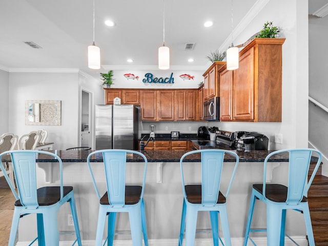 kitchen featuring a breakfast bar area, a peninsula, appliances with stainless steel finishes, brown cabinetry, and crown molding