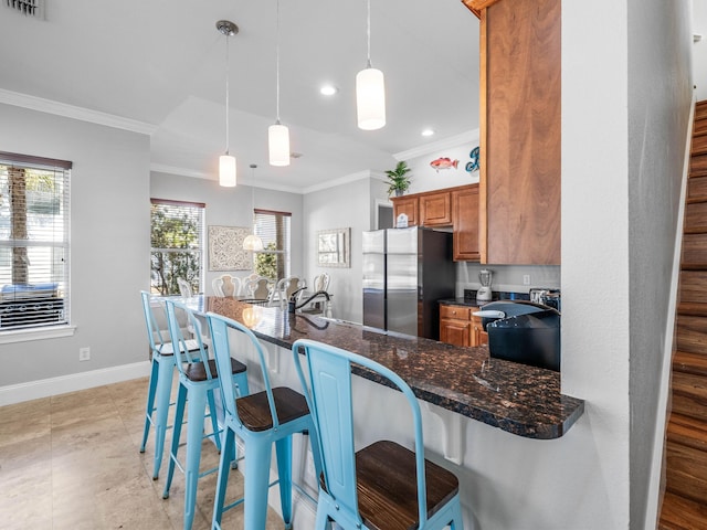 kitchen with baseboards, brown cabinets, freestanding refrigerator, a peninsula, and crown molding