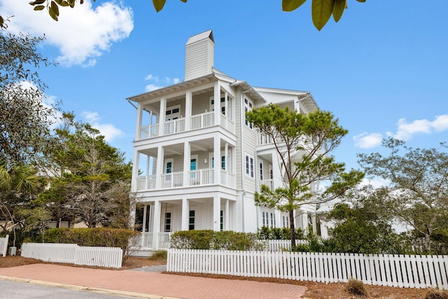 view of front of house with covered porch, a fenced front yard, a chimney, and a balcony