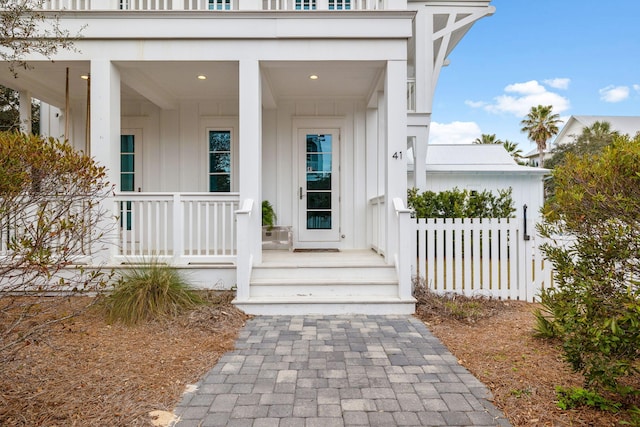 view of exterior entry with covered porch and fence