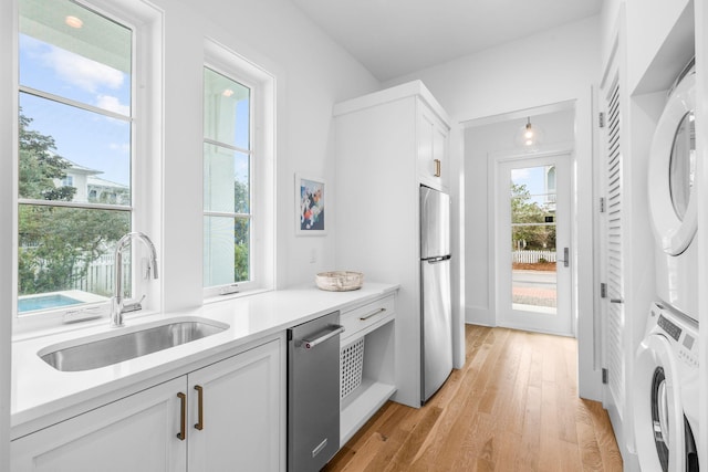 kitchen with light wood finished floors, stacked washer / drying machine, appliances with stainless steel finishes, white cabinetry, and a sink