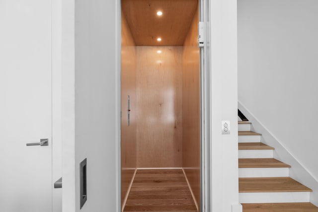 stairway with recessed lighting, wood finished floors, and elevator