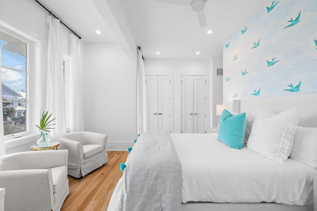 bedroom featuring baseboards, light wood finished floors, two closets, and recessed lighting