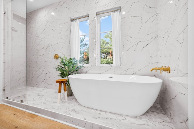 full bath with marble finish floor, stone wall, a soaking tub, and a marble finish shower