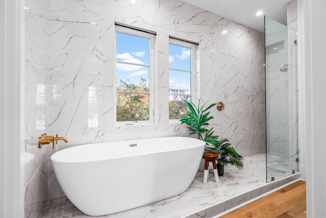 full bathroom with a marble finish shower, recessed lighting, wood finished floors, a freestanding tub, and stone wall