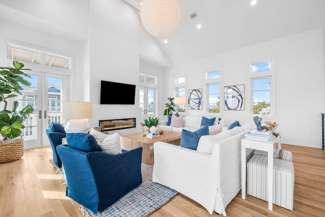 living room featuring visible vents, a glass covered fireplace, light wood-type flooring, high vaulted ceiling, and a wealth of natural light