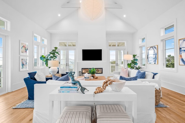 living area with high vaulted ceiling, light wood-type flooring, french doors, and a glass covered fireplace