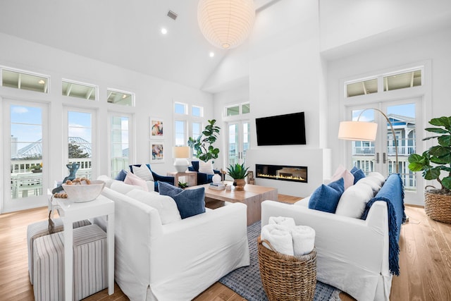 living room with light wood finished floors, plenty of natural light, high vaulted ceiling, and a glass covered fireplace