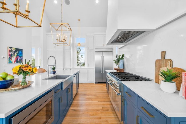 kitchen with built in appliances, a chandelier, a sink, white cabinets, and blue cabinetry