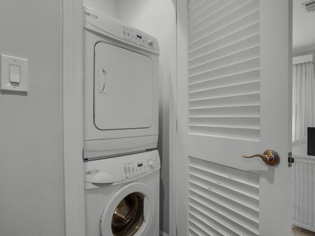 clothes washing area featuring stacked washer and clothes dryer, visible vents, and laundry area