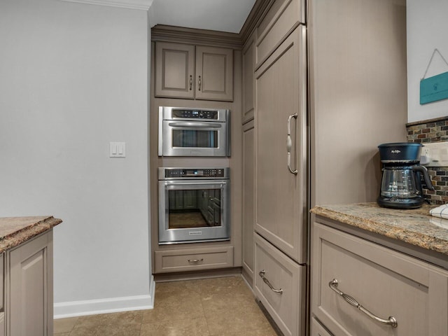 kitchen featuring light stone counters, backsplash, stainless steel double oven, light tile patterned flooring, and baseboards