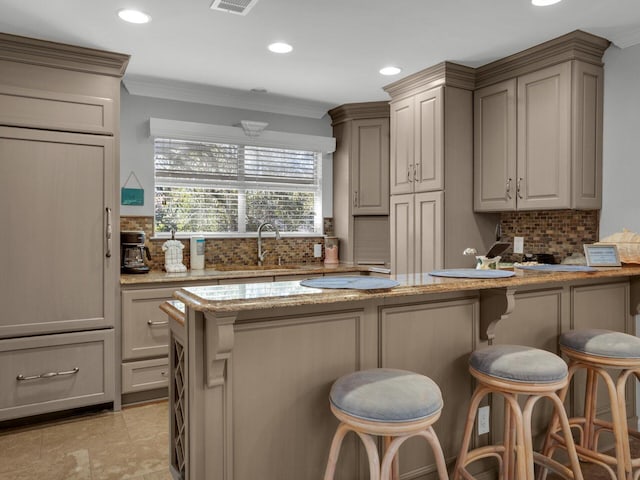 kitchen with light stone counters, a breakfast bar area, recessed lighting, backsplash, and a sink