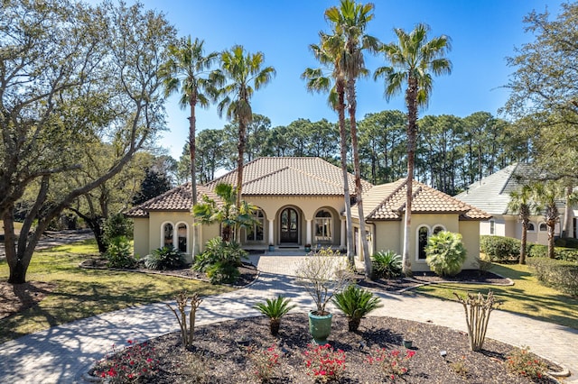 mediterranean / spanish-style house featuring driveway, a tiled roof, a front lawn, and stucco siding