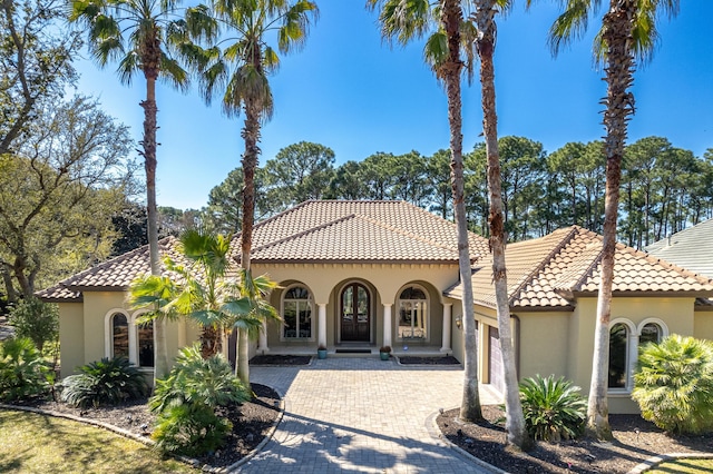 mediterranean / spanish house featuring an attached garage, a tiled roof, decorative driveway, and stucco siding