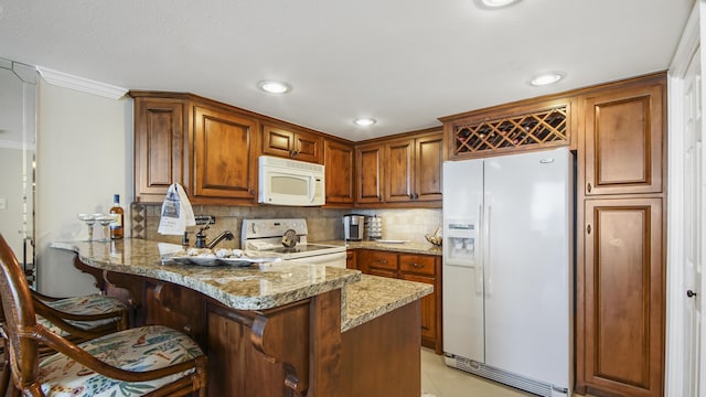 kitchen featuring backsplash, light stone countertops, a peninsula, brown cabinetry, and white appliances