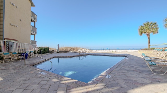 pool with a patio, a water view, and a view of the beach