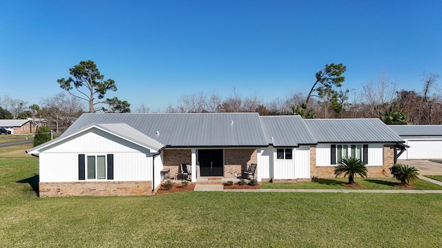 back of property featuring metal roof, a lawn, and brick siding