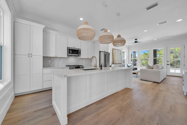 kitchen featuring stainless steel appliances, a sink, white cabinetry, open floor plan, and a center island with sink