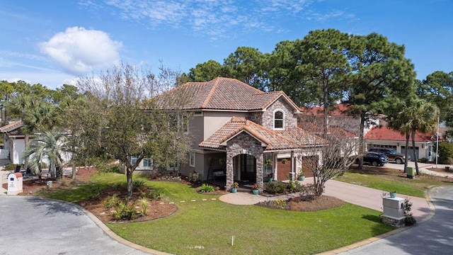 mediterranean / spanish home featuring a tile roof, stucco siding, concrete driveway, a front yard, and stone siding