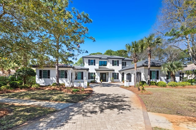 mediterranean / spanish-style home featuring decorative driveway, a front lawn, stucco siding, and a tiled roof