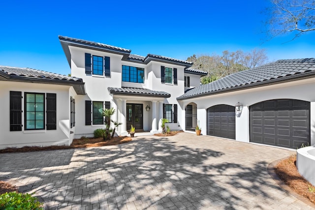 mediterranean / spanish house with stucco siding, a tiled roof, decorative driveway, and a garage