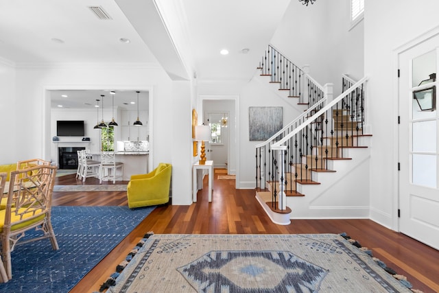 foyer with wood finished floors, visible vents, ornamental molding, stairs, and a glass covered fireplace