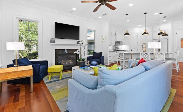 living area with visible vents, recessed lighting, dark wood-type flooring, a glass covered fireplace, and crown molding