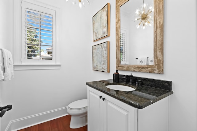 half bathroom featuring baseboards, toilet, wood finished floors, a notable chandelier, and vanity