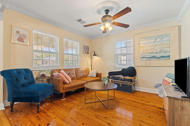 living area with light wood finished floors, visible vents, baseboards, a ceiling fan, and crown molding