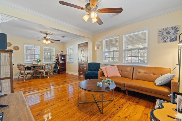 living room with ceiling fan, visible vents, baseboards, light wood-type flooring, and crown molding