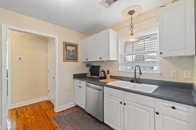 kitchen featuring stainless steel dishwasher, dark countertops, a sink, and white cabinets