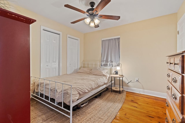 bedroom with a ceiling fan, baseboards, multiple closets, and wood finished floors