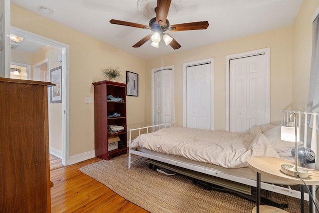 bedroom featuring a ceiling fan, light wood-type flooring, baseboards, and two closets