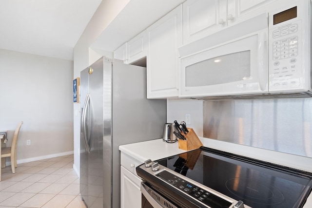 kitchen with light tile patterned floors, white microwave, light countertops, white cabinetry, and range with electric stovetop