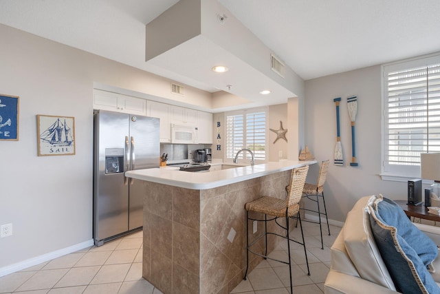 kitchen featuring a breakfast bar, stainless steel refrigerator with ice dispenser, white microwave, light tile patterned flooring, and a peninsula