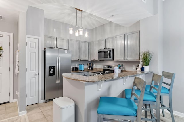 kitchen featuring stone counters, a breakfast bar, light tile patterned floors, appliances with stainless steel finishes, and a peninsula