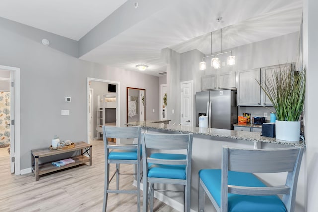 kitchen featuring light stone counters, light wood-type flooring, stainless steel fridge, a peninsula, and a kitchen breakfast bar