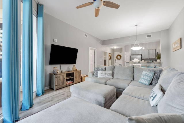 living room featuring light wood-style flooring, visible vents, and a ceiling fan