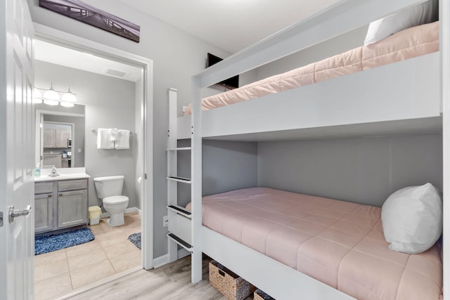 bedroom featuring light tile patterned floors, visible vents, ensuite bathroom, a sink, and baseboards