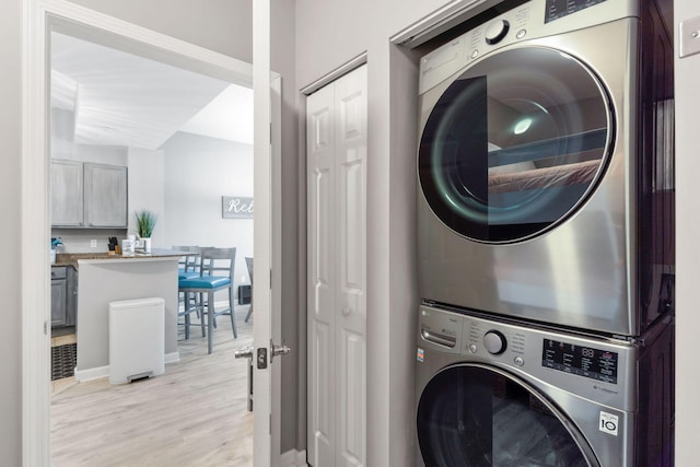 clothes washing area with light wood-type flooring, laundry area, and stacked washer / dryer