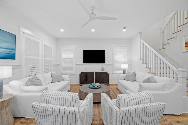 living area featuring wainscoting, ceiling fan, stairway, wood finished floors, and crown molding