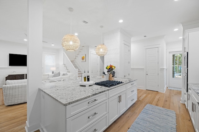 kitchen with light stone counters, light wood-style flooring, white cabinets, appliances with stainless steel finishes, and wainscoting