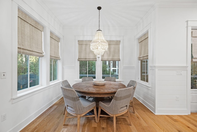 dining space with ornamental molding, a chandelier, a wainscoted wall, and light wood finished floors